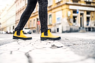 Gambe di una donna con stivali gialli che cammina per strada in città.