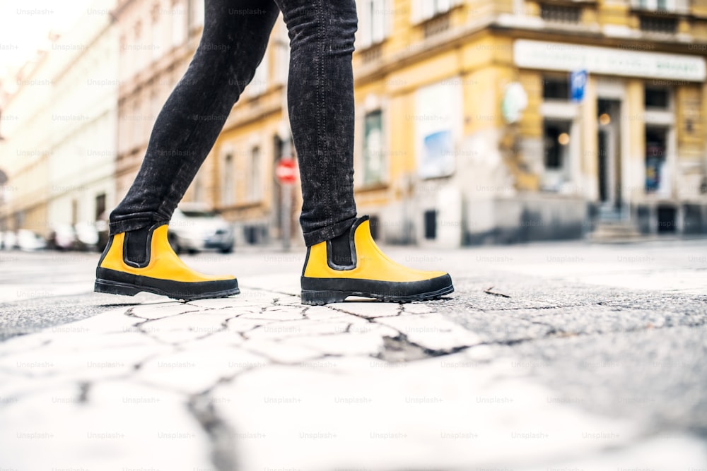 Beine einer Frau mit gelben Stiefeln, die auf der Straße in der Stadt läuft.