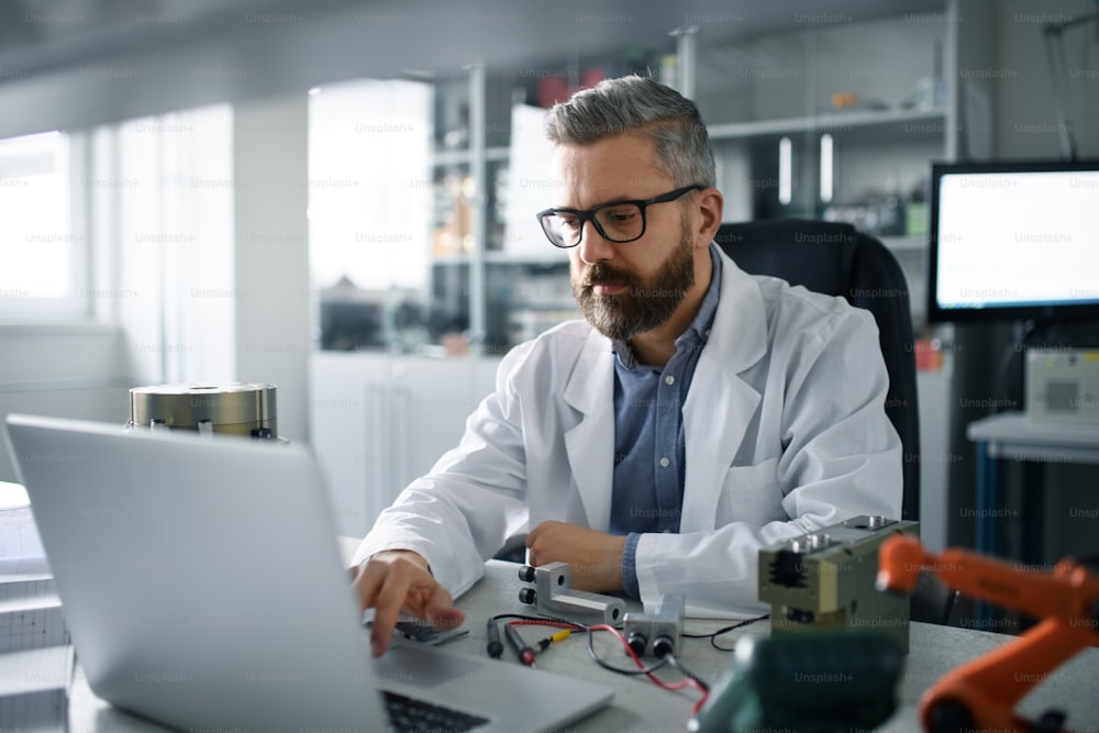 A robotics engineer working on desing of modern robotic arm aand sitting at desk in laboratory.