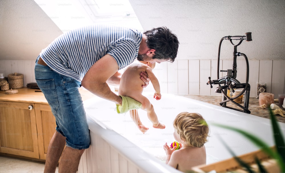 Father washing two toddlers in the bath in the bathroom at home. Paternity leave.