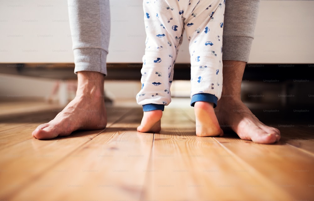 自宅の寝室の床に立っている見分けのつかない父親とよちよち歩きの男の子の足。育児休暇。スペースをコピーします。