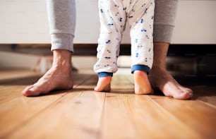 Gambe di padre irriconoscibile e un bambino in piedi sul pavimento nella camera da letto di casa. Congedo di paternità. Copia spazio.