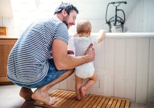 Father with a toddler child at home standing by the tub in the bathroom. Paternity leave.