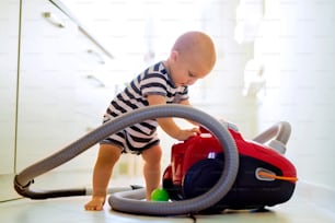Cute baby boy with the hoover in the kitchen. Close up of a little boy playing with vacuum cleaner.