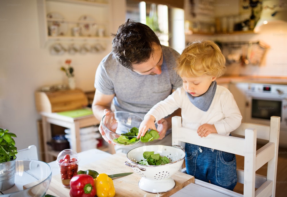 よちよち歩きの男の子と料理をする若い父親。野菜サラダを作る息子と男性。