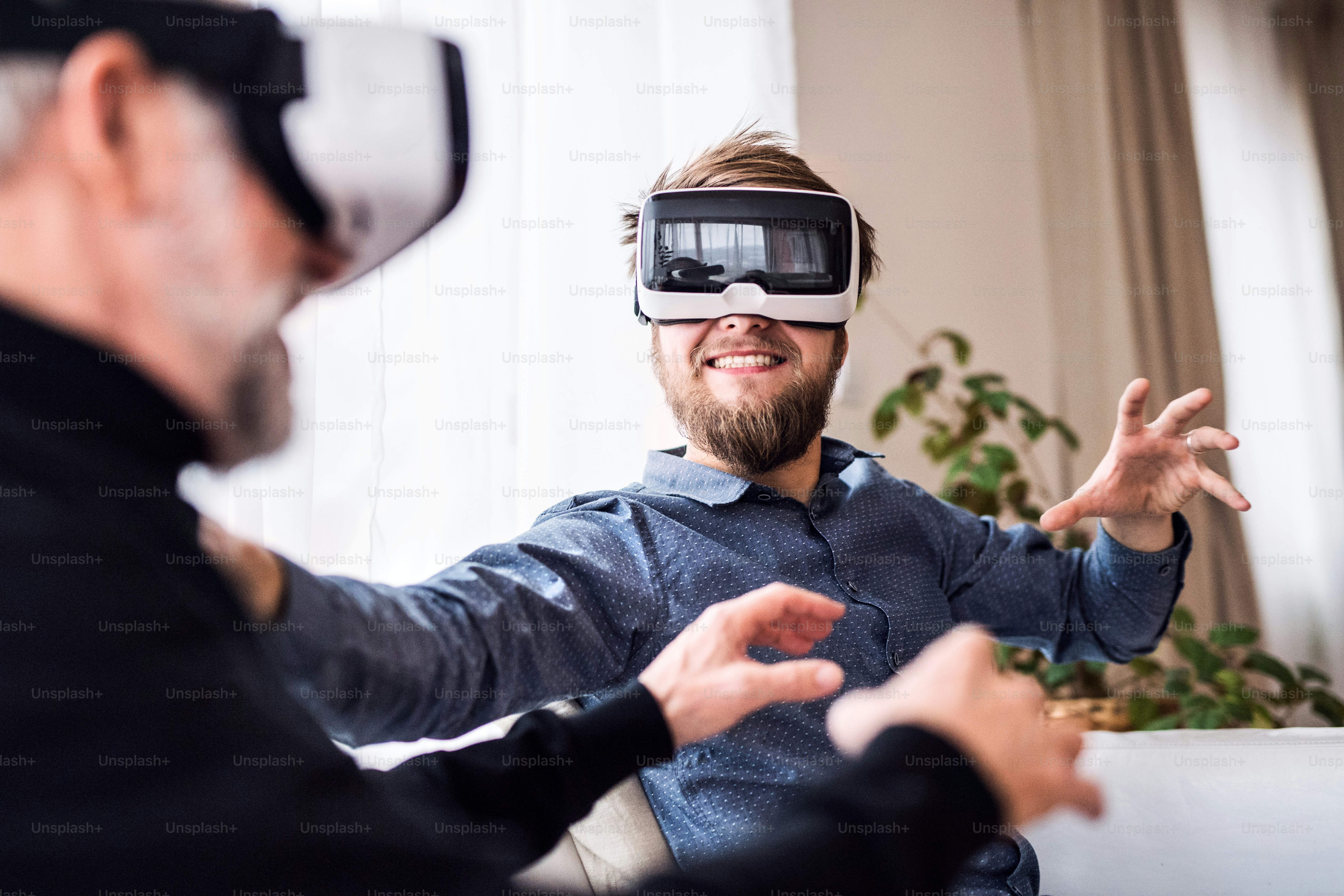 Hipster son and his senior father with VR goggles at home. Two generations indoors, having fun.