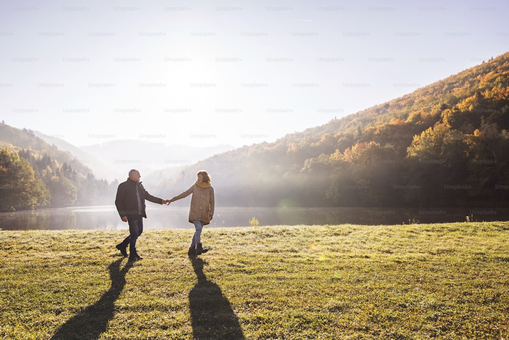 Active senior couple on a walk in a beautiful autumn nature. A man and woman by the lake in the early morning.