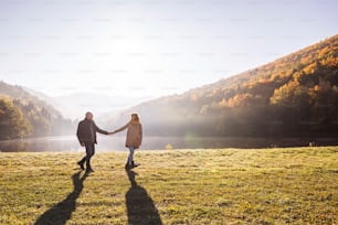 Active senior couple on a walk in a beautiful autumn nature. A man and woman by the lake in the early morning.