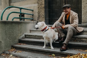 Un uomo anziano felice seduto sulle scale e che riposa durante la passeggiata con il cane all'aperto in città.