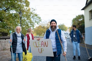 Un groupe diversifié de bénévoles heureux marchant avec des banderoles et des outils pour nettoyer les rues.