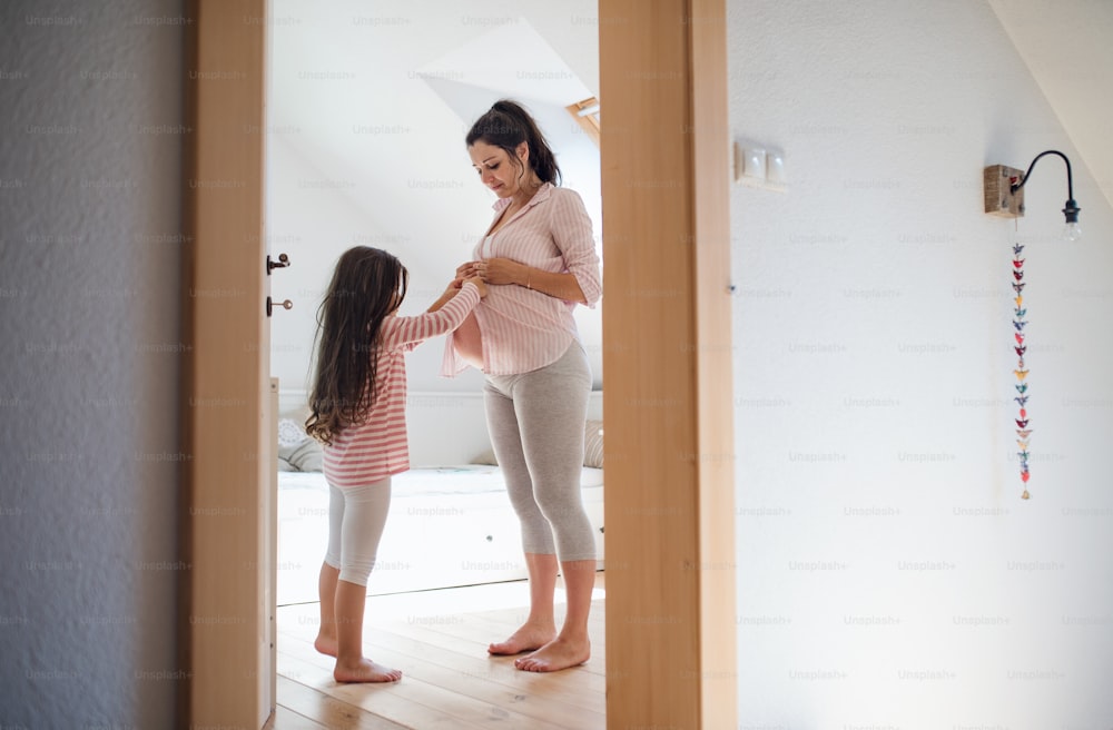 Side view portrait of pregnant woman with small daughter indoors in bathroom at home.