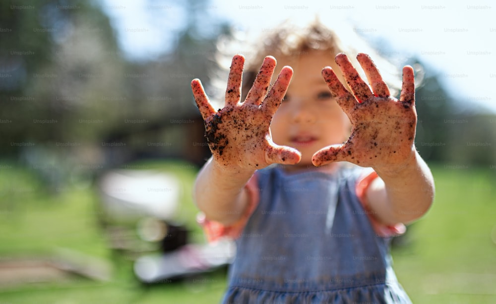 Retrato de una niña pequeña que muestra las manos sucias al aire libre en el jardín, concepto de estilo de vida sostenible.