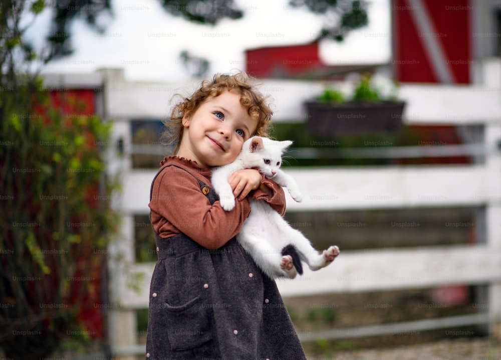 Ritratto di piccola ragazza con gatto in piedi sulla fattoria, guardando la macchina fotografica.