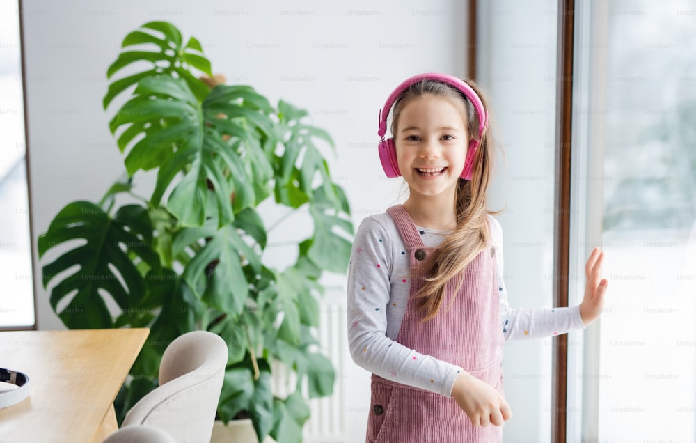 Small girl with headphones standing indoors at home, looking at camera.