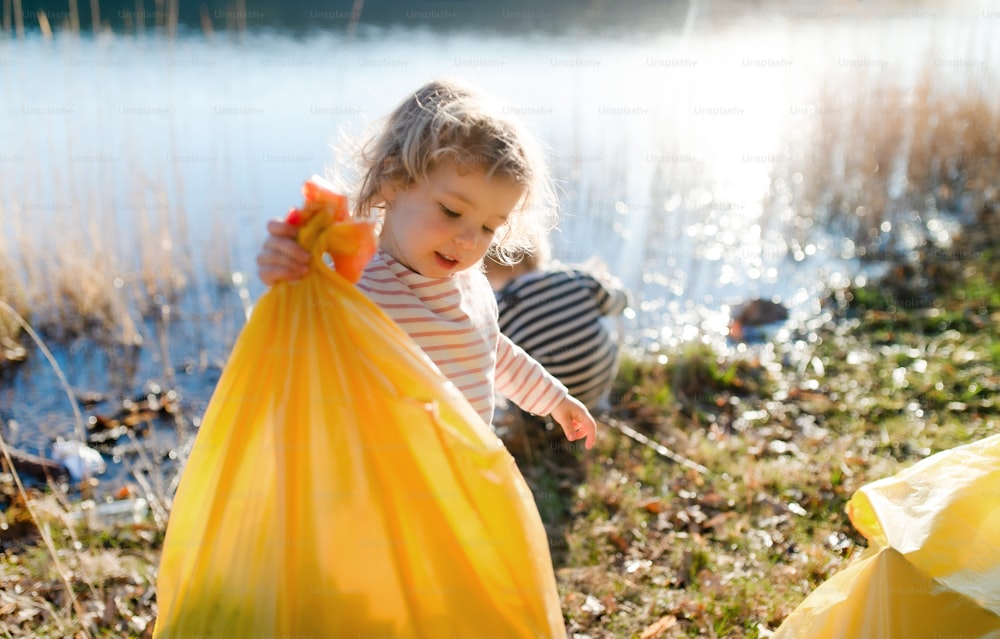 Petits enfants ramassant des ordures à l’extérieur au bord d’un lac dans la nature, concept de plogging.