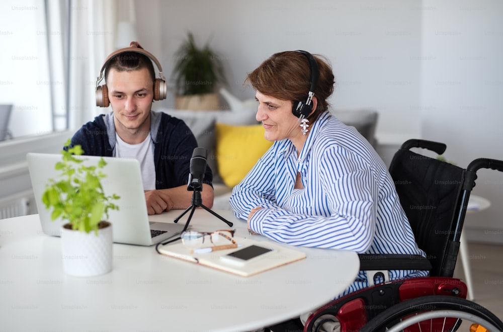 Happy disabled people sitting at the table indoors at home, recording podcast at home.