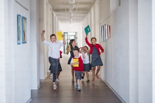 A group of cheerful small school kids in corridor, running and jumping. Back to school concept.