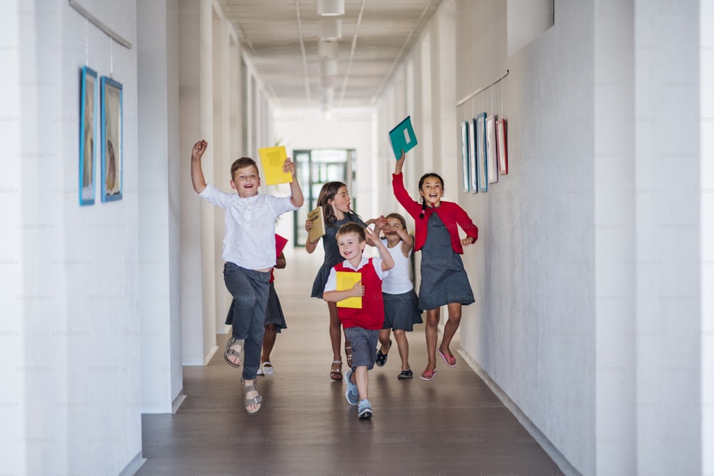 Un gruppo di allegri bambini della scuola nel corridoio, che corrono e saltano. Concetto di ritorno a scuola.