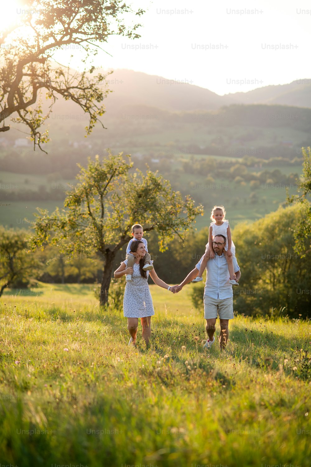 해질녘 야외 초원을 걷고 있는 두 명의 어린 자녀와 함께 피기백 타기를 하는 가족의 전면 보기.