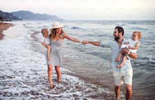 Eine junge Familie mit zwei Kleinkindern, die im Sommerurlaub am Strand spazieren gehen.