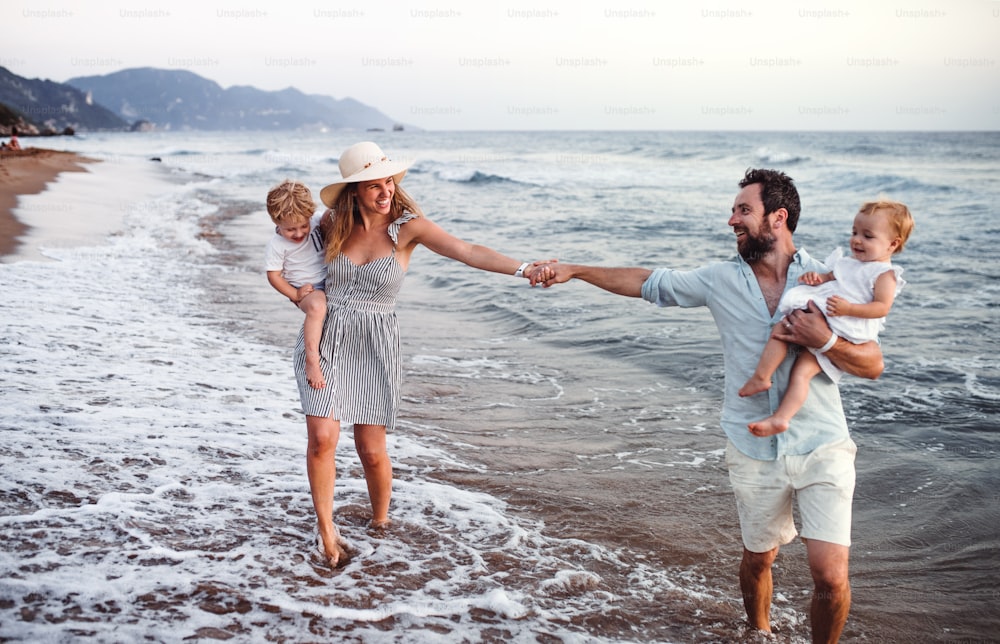 A young family with two toddler children walking on beach on summer holiday.