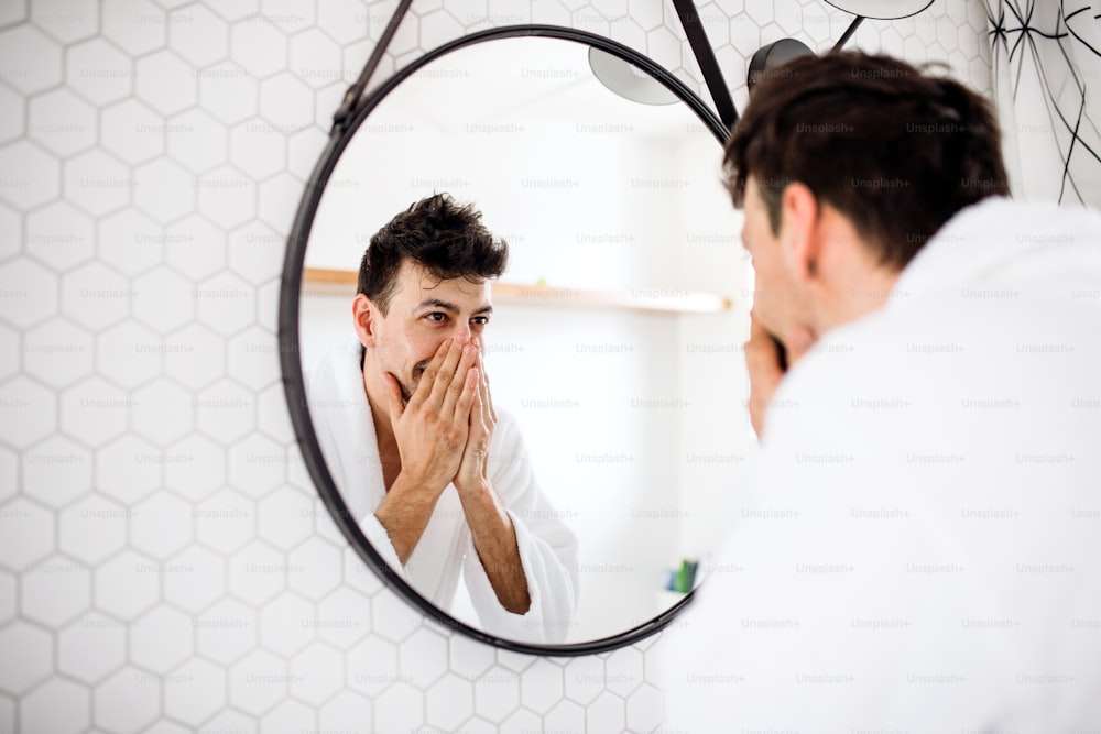 A young man looking in mirror in the bathroom in the morning, daily routine.