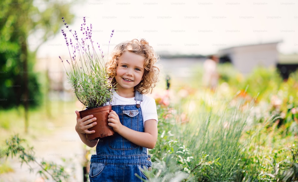 Portrait of small girl standing in the backyard garden, holding a plant in a pot. Copy space.