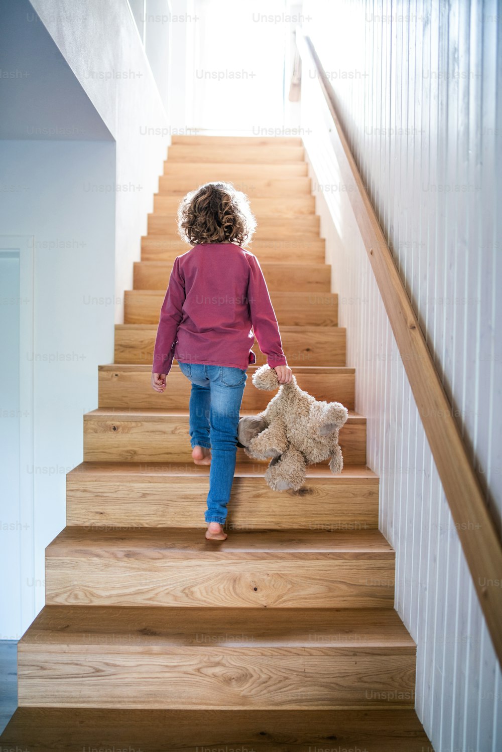 A rear view of small girl walking up wooden stairs indoors at home. Copy space.
