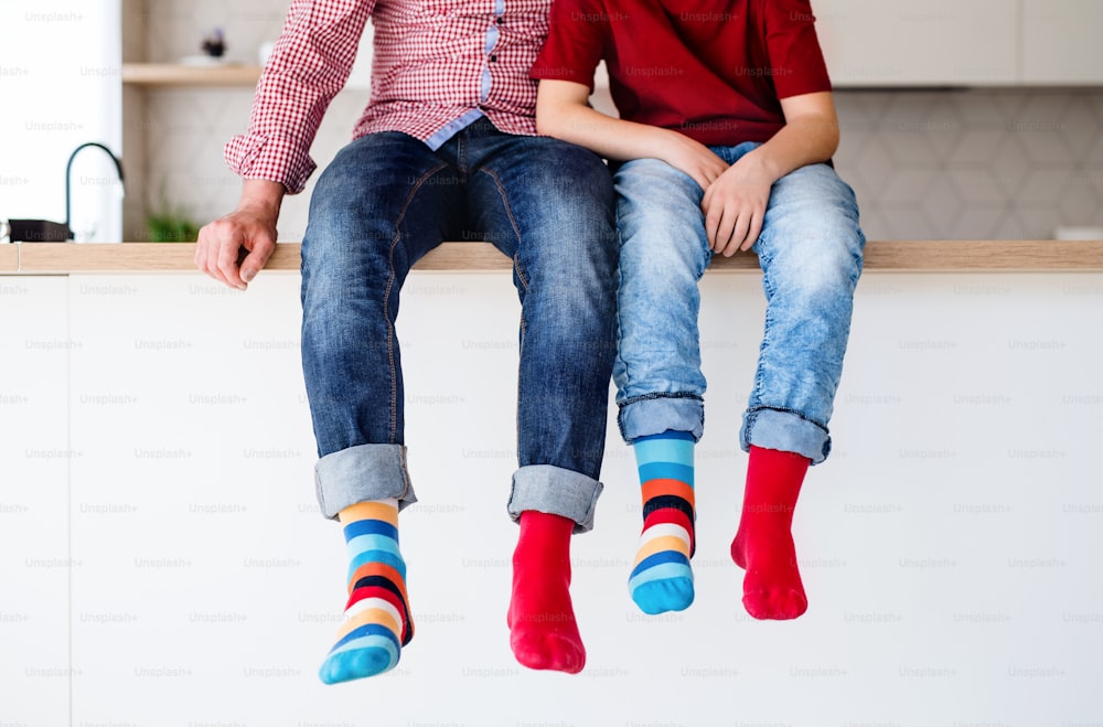 Midsection of father with small son with funky socks sitting on kitchen counter indoors.