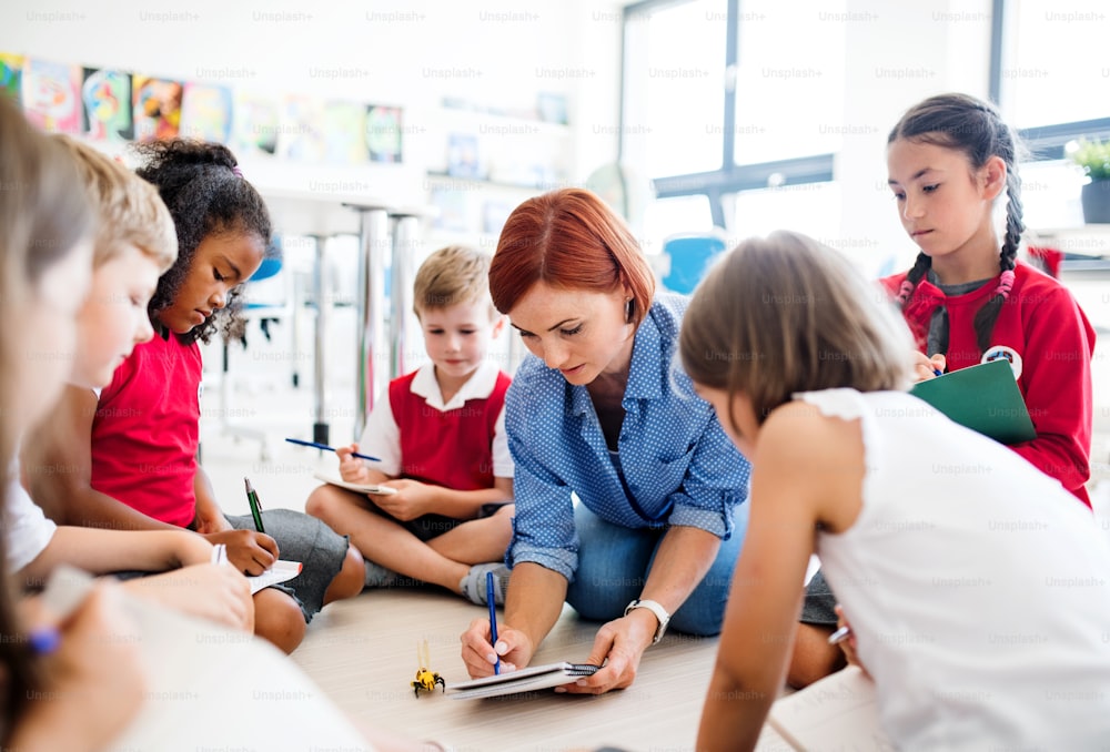 Um grupo de crianças pequenas da escola com o professor sentado no chão em sala de aula, aprendendo ciências.
