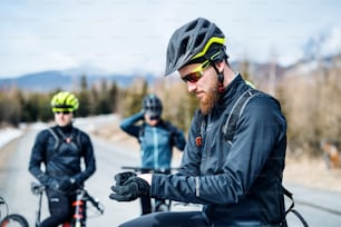 A group of young mountain bikers standing on road outdoors in winter.