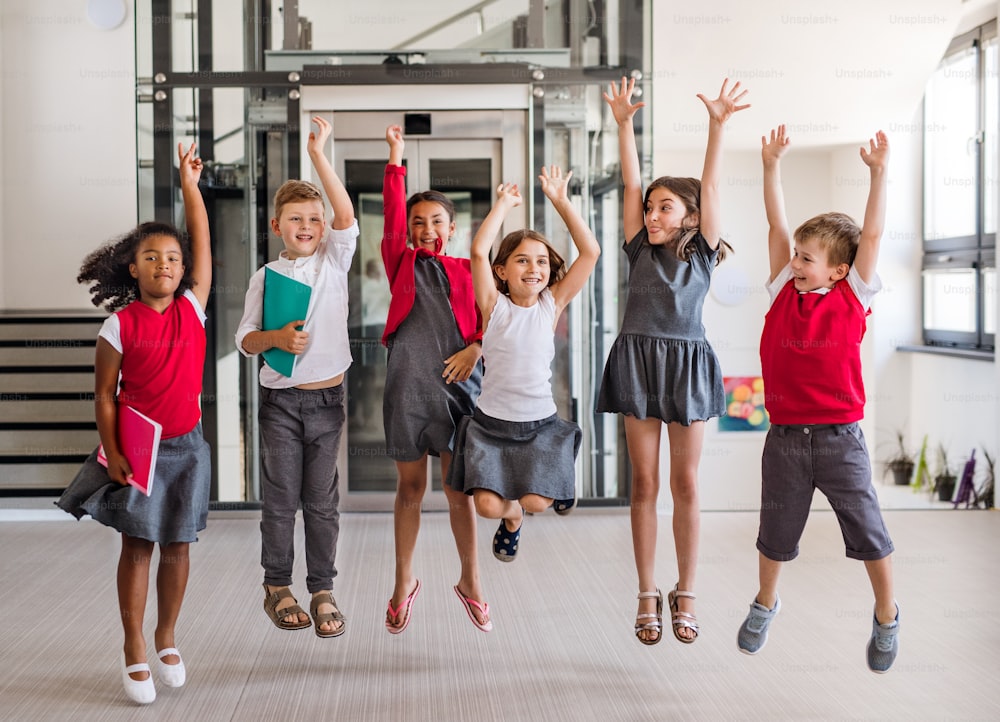 Eine Gruppe fröhlicher kleiner Schulkinder im Flur, springend. Back to School Konzept.