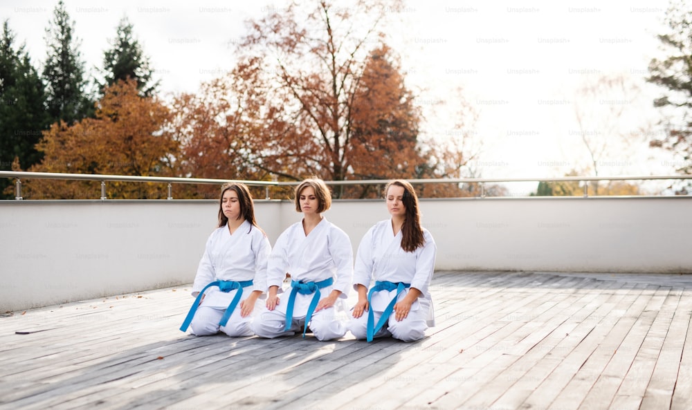 屋外のテラスに座って瞑想している若い空手の女性のグループ。