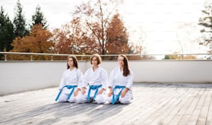 A group of young karate women sitting outdoors on terrace, meditating.