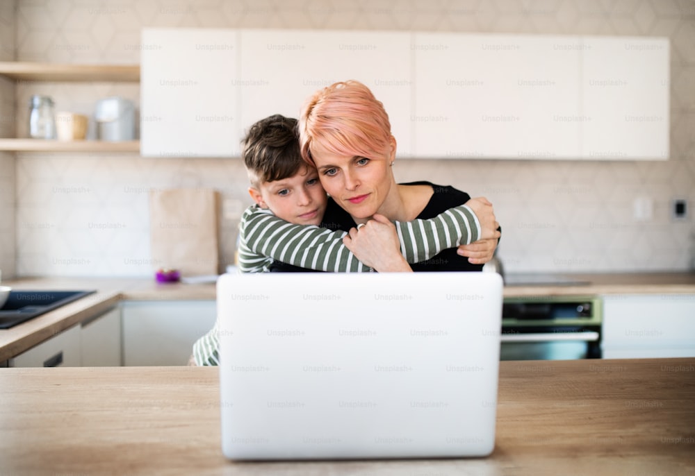 Eine junge Frau mit einem kleinen Sohn, der zu Hause in einer Küche einen Laptop benutzt und arbeitet.