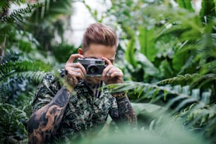 Un joven con una cámara de pie en el jardín botánico, tomando fotografías.
