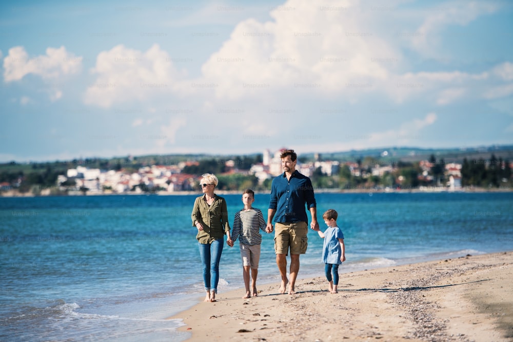 Junge Familie mit zwei kleinen Kindern, die barfuß im Freien am Strand spazieren gehen.
