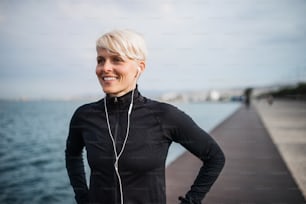 Retrato de vista frontal de una joven deportista con auriculares de pie al aire libre en la playa.