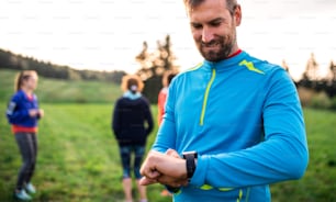 A portrait of man with large group of people doing exercise in nature, using smartwatch.