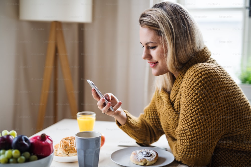 自宅で屋内のテーブルに座り、リラックスするときにスマートフォンを使用する若い女性。