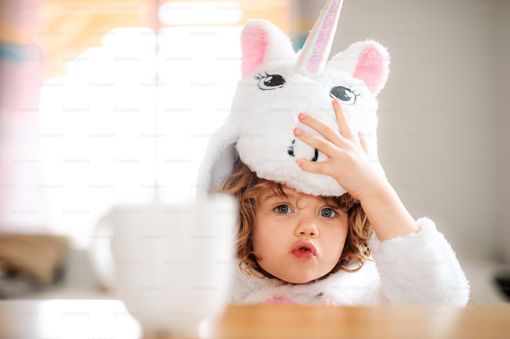 Un retrato de una niña feliz con máscara de unicornio sentada en la mesa de casa.