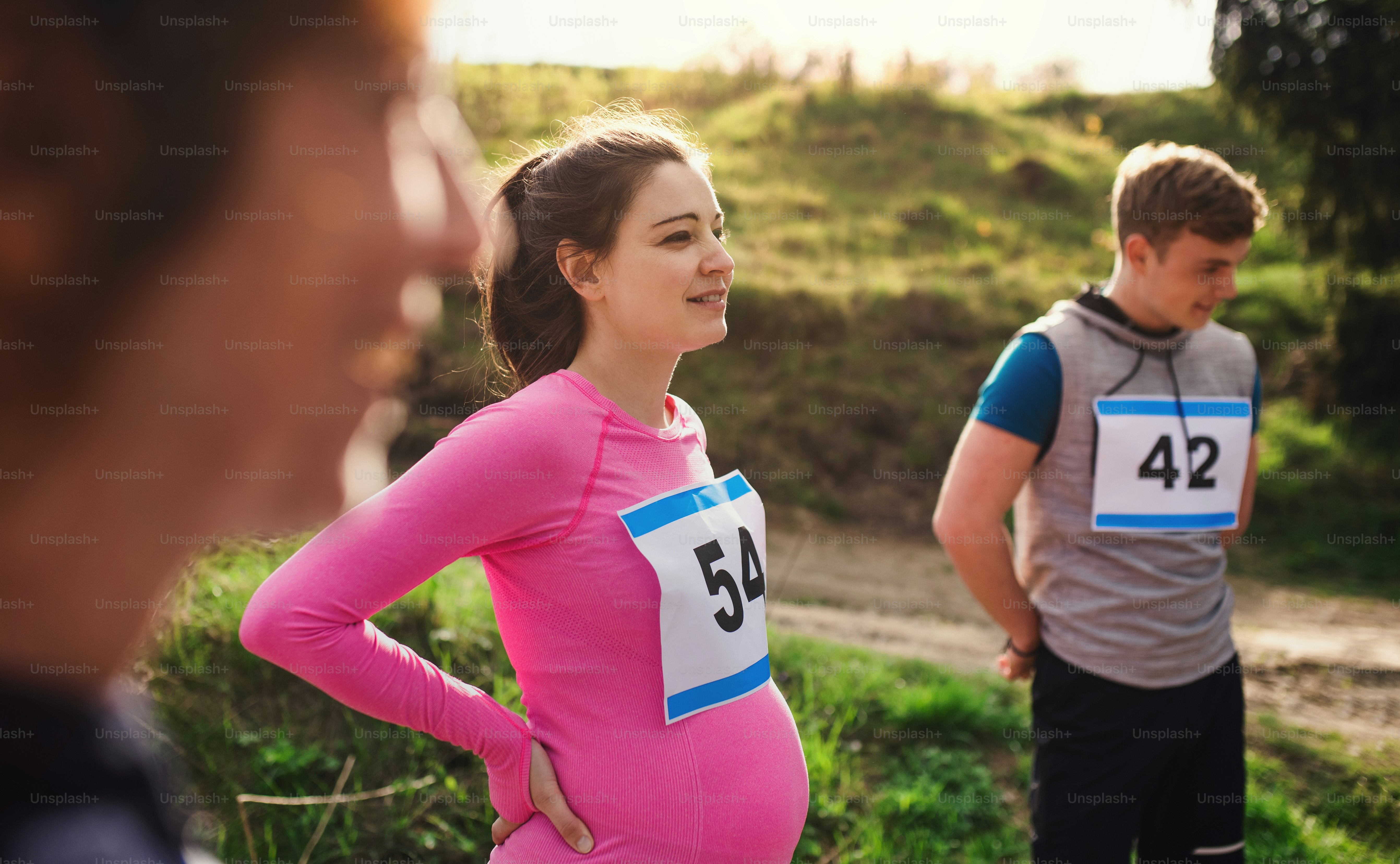 Fit and active pregant woman with friends doing exercise in nature, resting.