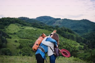 A young tourist couple travellers with backpacks hiking in nature, hugging.