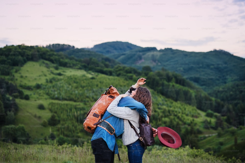 Una joven pareja de turistas viajeros con mochilas caminando por la naturaleza, abrazándose.