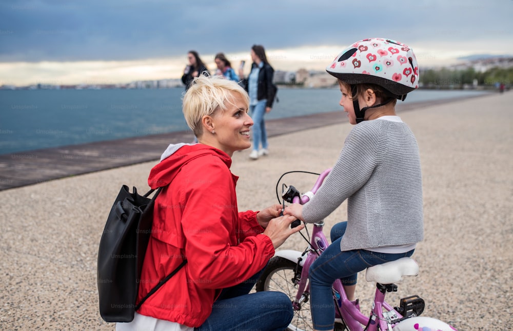 A mother and small daughter with bicycle outdoors on beach, talking.
