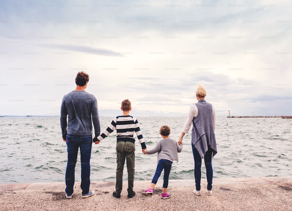Vista trasera de una familia joven con dos niños pequeños de pie al aire libre en la playa, tomados de la mano.