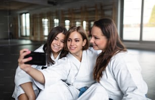 Group of young karate women with smartphone indoors in gym, taking selfie.