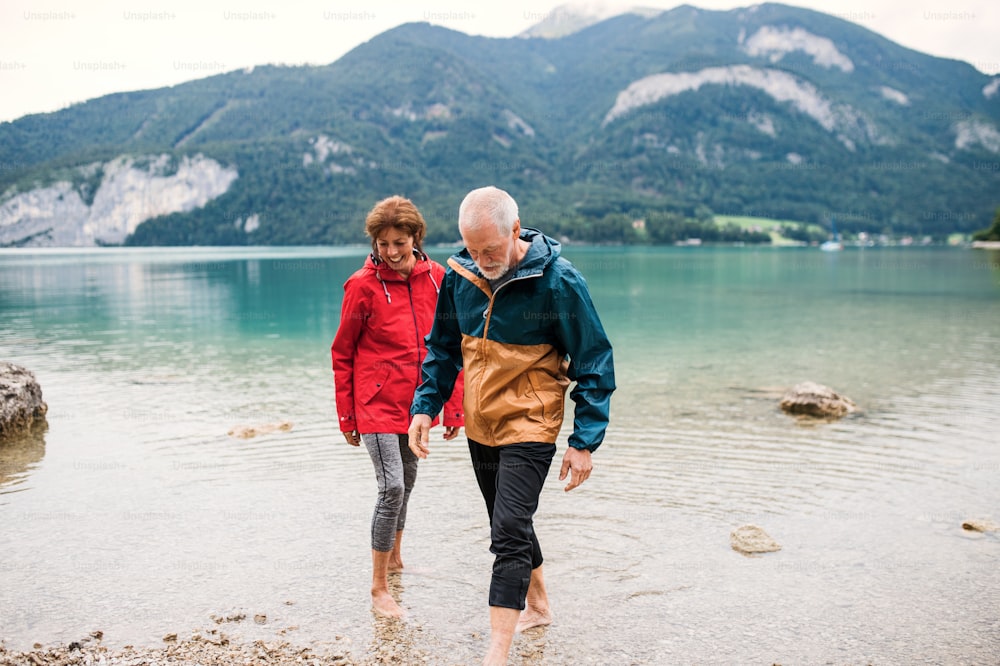 Una pareja de jubilados mayores excursionistas de pie descalzos en un lago de montaña en la naturaleza.