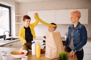 A happy young woman with two children unpacking shopping in a kitchen.