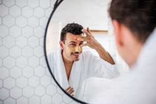 Young man putting mask on face in the bathroom in the morning, a daily routine.